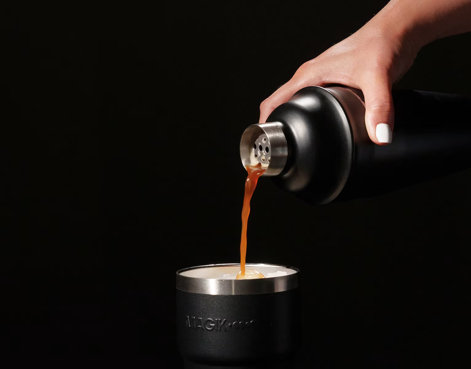 Hand pouring coffee from a black and silver container into a matching cup on a black background