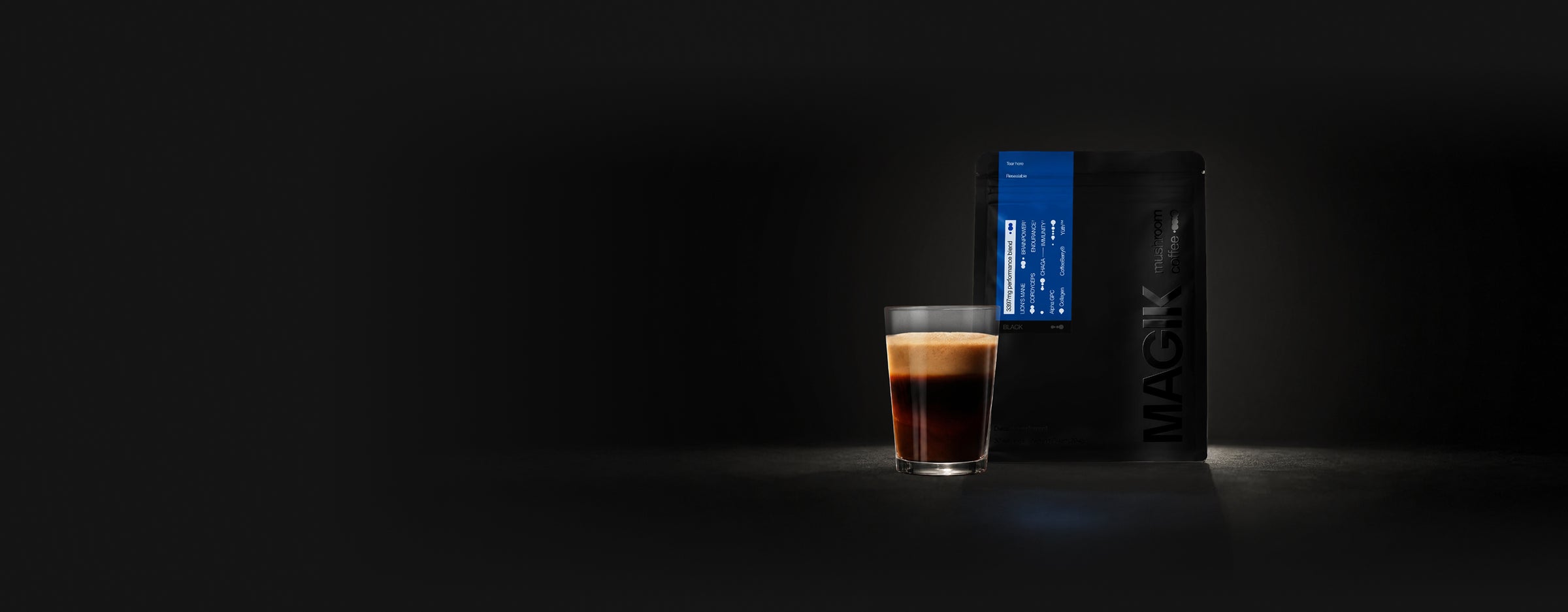 Glass of coffee and Magik Mushroom coffee packaging on a dark background